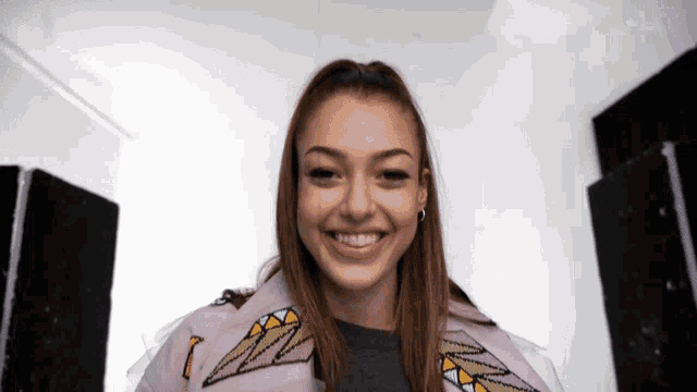 a woman wearing a pink jacket with triangles on the sleeves smiles at the camera