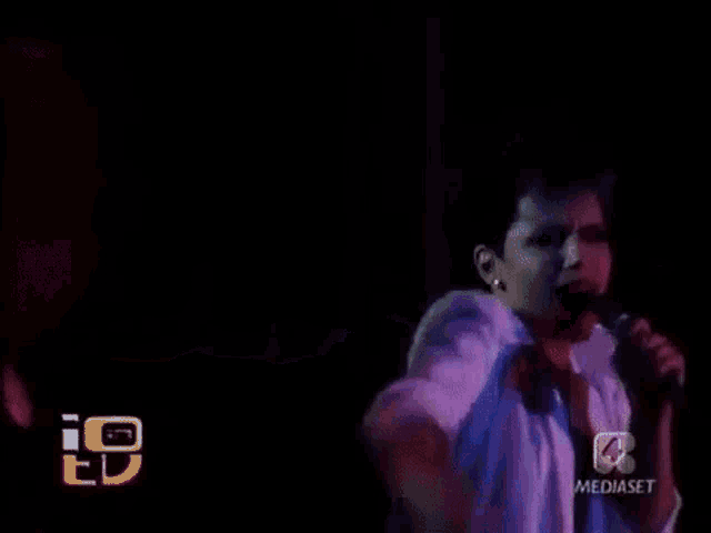 a man is singing into a microphone in a dark room with his arms outstretched .