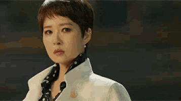 a woman with short hair is wearing a white coat and a black polka dot shirt .