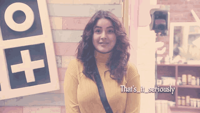 a woman in a yellow sweater is standing in front of a sign that says " that 's it seriously "