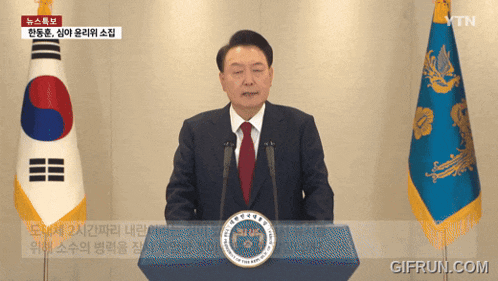 a man in a suit and tie stands at a podium in front of two flags with ytn written on the bottom right