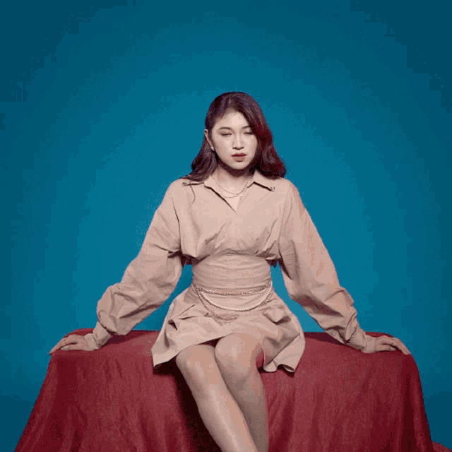 a woman in a tan dress is sitting on a red blanket