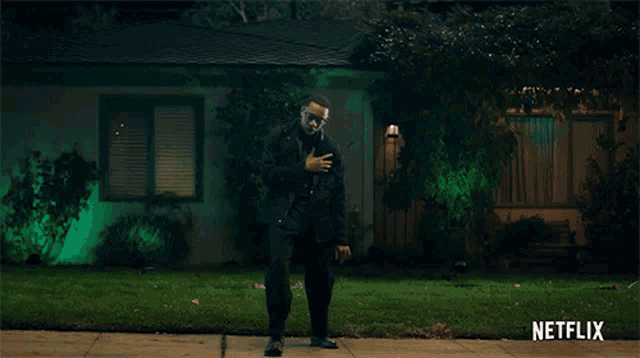 a man in a tuxedo is standing in front of a house that has green lights on