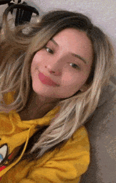 a woman wearing a yellow hoodie with mickey mouse on it smiles for the camera