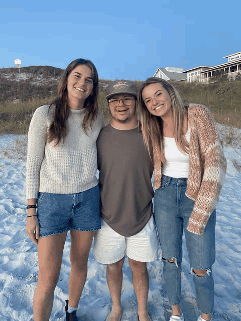 three people posing for a picture on a beach with one wearing a hat that says florida on it