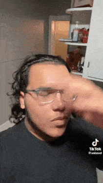 a man wearing glasses and a black shirt is holding his nose .