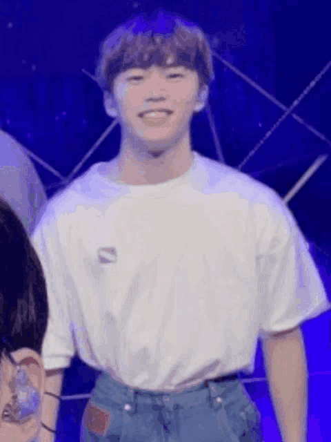 a young man is wearing a white t-shirt and blue jeans .