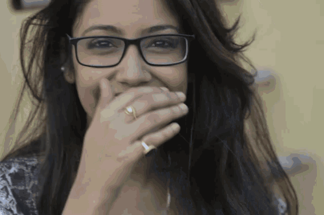 a woman wearing glasses and a gold ring covers her mouth