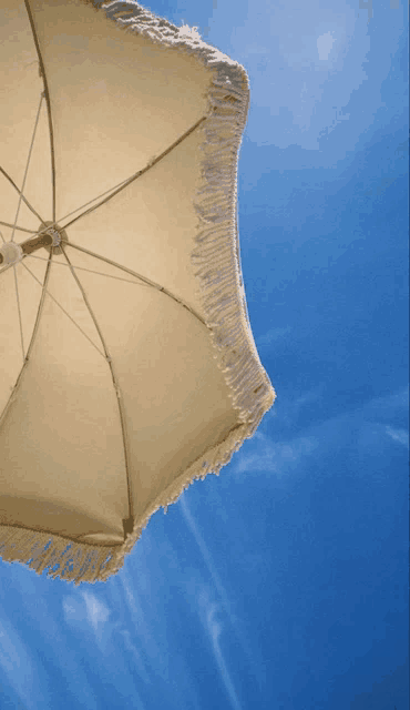 a white beach umbrella with fringe against a blue sky