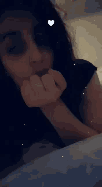 a woman is laying on a bed with her hand on her face and a heart in the background .