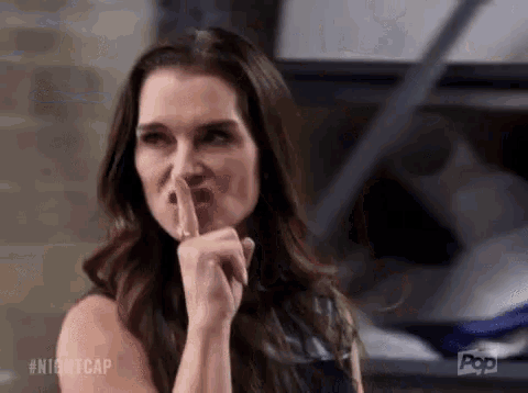 a woman is holding her finger to her lips and making a shhh gesture .