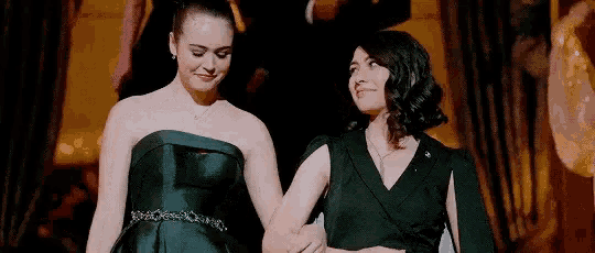 two women in black dresses are standing next to each other in a room holding hands .