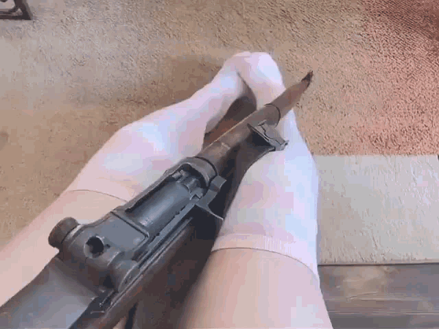 a person wearing pink socks is holding a gun between their legs .