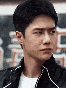 a close up of a young man 's face with a black jacket on .