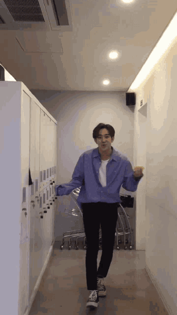 a man in a purple shirt and black pants is standing in a hallway