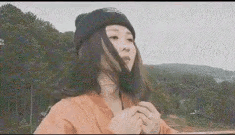 a woman wearing a beanie and a choker is standing in front of a mountain .