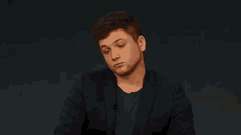 a man in a suit and blue shirt is sitting down and making a funny face .