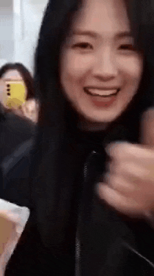a woman with long black hair is smiling while holding a cell phone in her hand .
