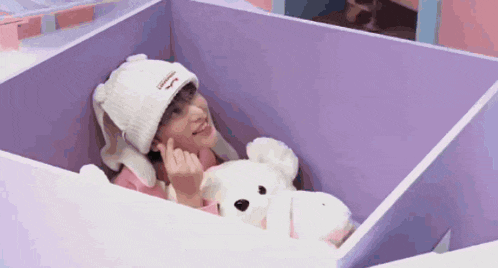 a person is laying in a box with a teddy bear .