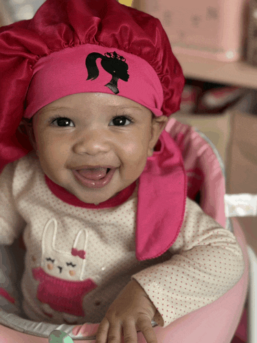 a baby wearing a pink satin hat with a barbie logo on it