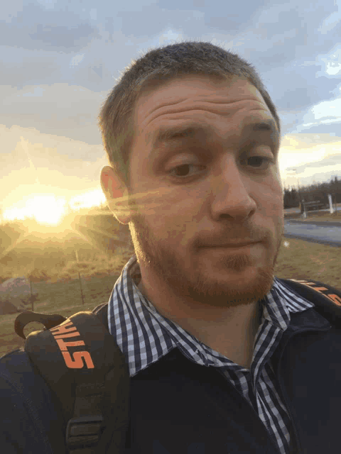 a man wearing a stihl backpack stands in front of a sunset