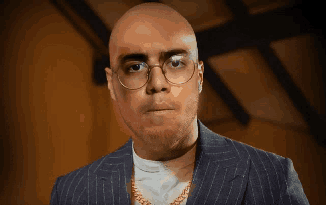 a bald man wearing glasses and a gold chain