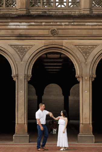 a man and woman are holding hands in front of a stone archway