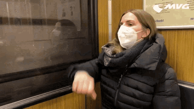 a woman wearing a mask is looking out a window with a sign that says mvg behind her