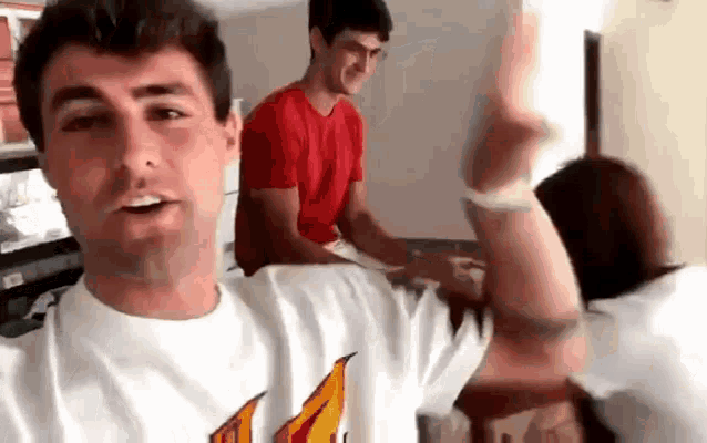 a man in a white t-shirt is taking a selfie with two other men in a living room .