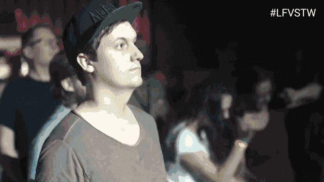 a man wearing a hat that says ' alex ' on it stands in a crowd of people