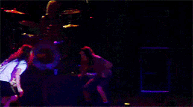 a man in a white shirt is dancing on a stage with a drum set in the background