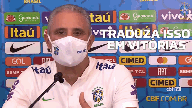 a man wearing a face mask stands in front of a banner that says itau