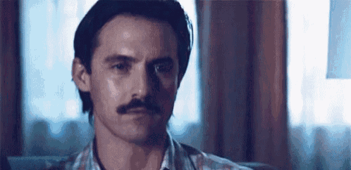 a man with a mustache is sitting on a couch .