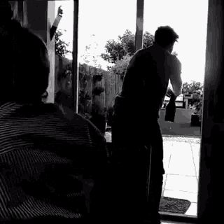 a black and white photo of a man standing in front of a glass door .