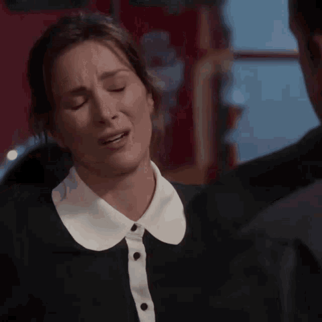 a woman in a black dress with a white collar is crying .