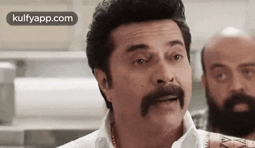a man with a mustache is making a funny face while standing next to another man .