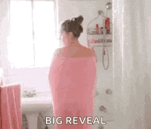 a woman wrapped in a pink towel is standing in a bathroom next to a sink .
