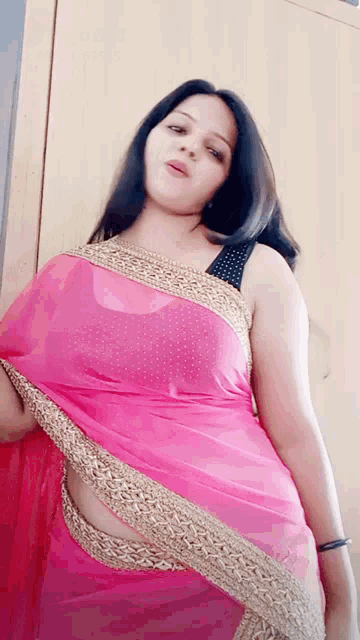 a woman in a pink saree is standing in front of a cabinet