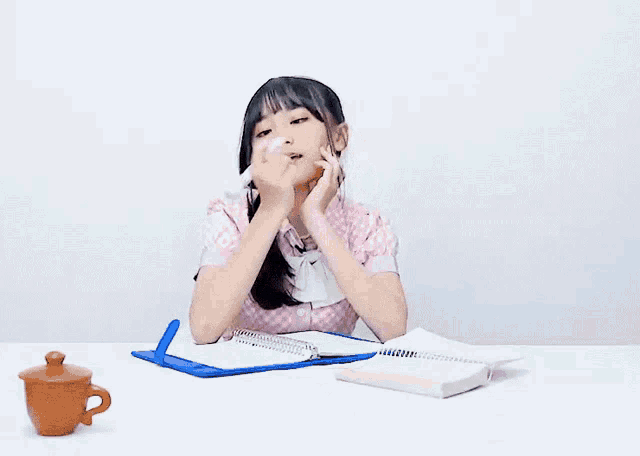 a girl sitting at a desk with a book and a cup