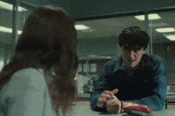 a man and a woman are sitting at a table and the man is holding a bag of potato chips