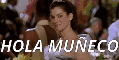 a woman in a white dress is smiling in front of a crowd and the words hola muneco are on the screen .