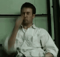 a man in a white shirt is sitting in a chair with his hand on his nose .