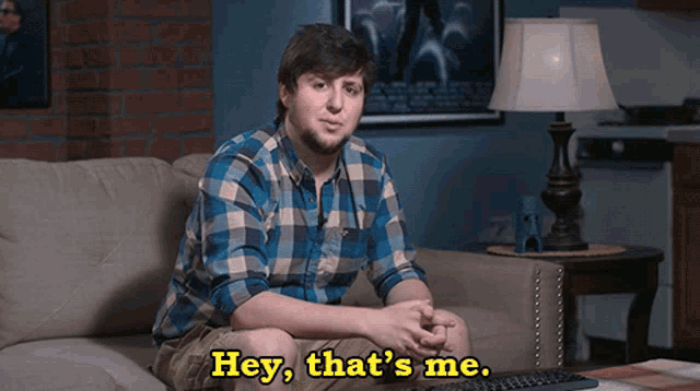 a man in a plaid shirt sits on a couch with the words hey that 's me above him