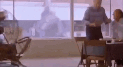 a man is standing in front of a window in a room talking to a woman .