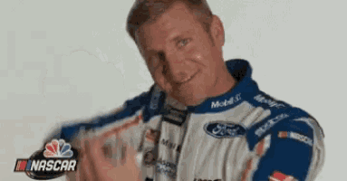 a man in a nascar uniform is smiling and holding a bottle .