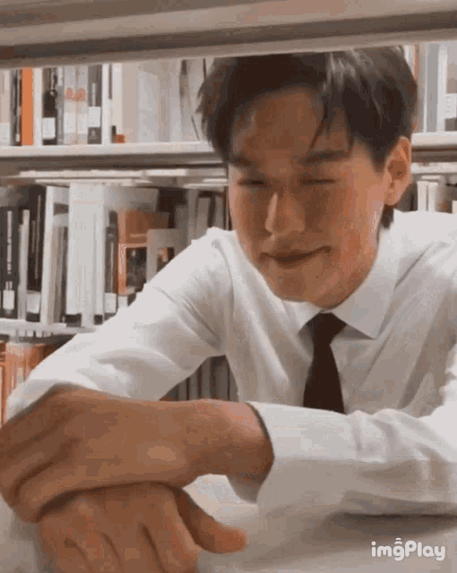 a man in a white shirt and tie is sitting under a bookshelf