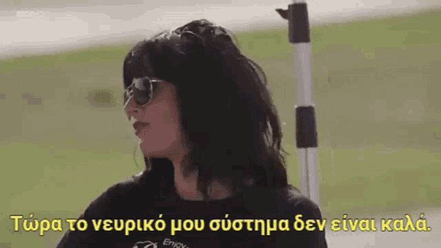 a woman wearing sunglasses and a black shirt is standing in front of a green field .
