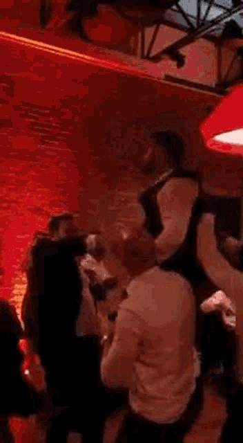 a group of people are dancing in a room with a red light on the ceiling .