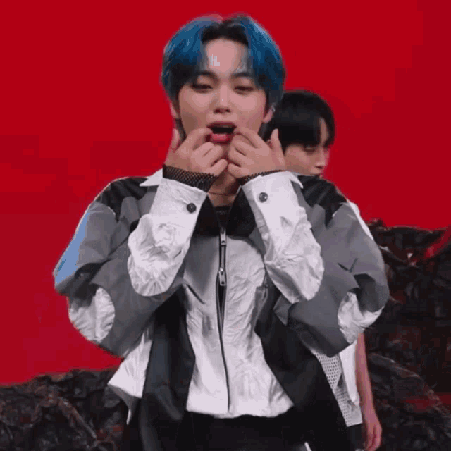 a young man with blue hair is making a heart shape with his hands