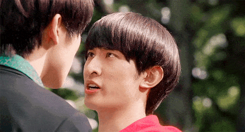 two young men looking at each other with one wearing a red sweater